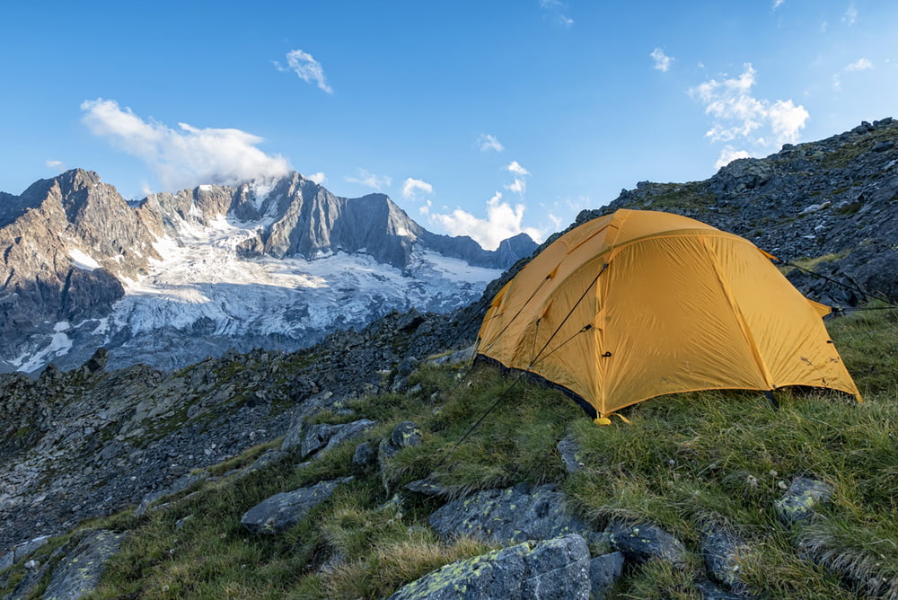 Gelbes Trekkingzelt auf alpinem Biwakplatz vor imposanter Bergkulisse mit Gletscher im Hintergrund